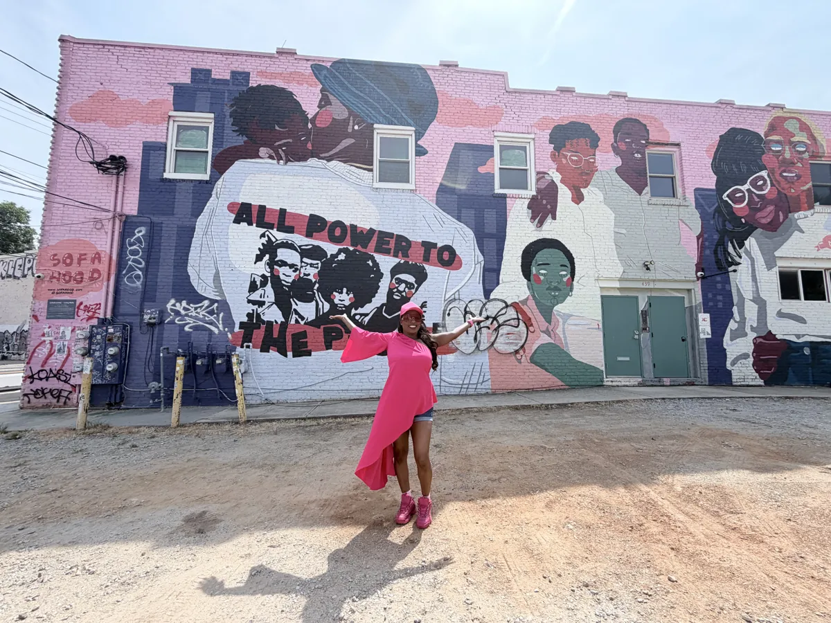 Guest posing in front of an All Power to the People mural in Atlanta
